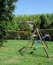 Columpios en un parque rodeado de árboles y césped verde bajo un cielo azul.