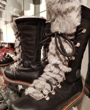 Schwarze Stiefel mit Fellbesatz und Schnürung, ausgestellt in einem Geschäft auf Glasregal.