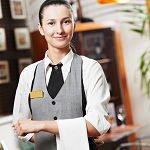 Smiling waitress in uniform with arms crossed, standing in a restaurant setting.