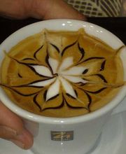 Tazza di cappuccino con decorazione floreale in latte art. Mano che regge la tazza bianca.