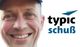 Lächelnder Mann mit Mütze neben dem Wort "typic schuß" und einem blauen Logo.