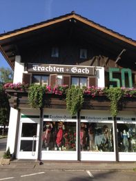 Zweistöckiges Haus mit Blumen, Schildern "Trachten Gach" und Schaufenster mit Trachtenmode.