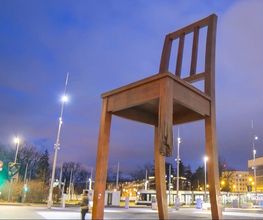Großer Holzstuhl mit einem gebrochenen Bein auf einem Platz bei Abenddämmerung.