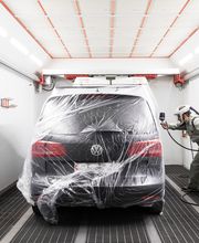 Auto wird in Lackierkabine von Person in Schutzanzug lackiert.