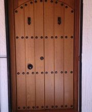 Puerta de madera estilo rústico con clavos de hierro negros y arco superior decorativo.