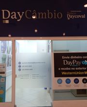 Fachada de uma agência de câmbio DayCâmbio, com adesivos promocionais na janela de entrada.