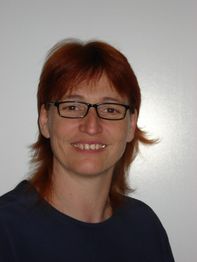 Eine lächelnde Person mit Brille vor einem neutralen Hintergrund.