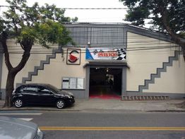 Fachada de um prédio com portão aberto e um carro preto estacionado na calçada.