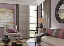 Elegant living room with beige sofa, patterned armchair, abstract art, and floor-to-ceiling windows.