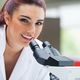 Woman in a lab coat smiling beside a microscope in a laboratory setting.