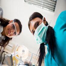 Two dental professionals in masks and goggles, looking down at a patient.