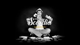 Magicien assis, montrant des cartes dans un spectacle de magie sur fond noir.