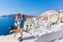 Paar tanzt auf Santorini mit weiß-blauen Häusern im Hintergrund, Blick aufs Meer.