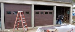 Three brown garage doors, a red ladder, and a person working on the right side.