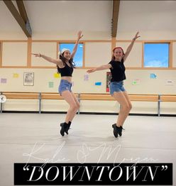 Two dancers in a studio, leaping joyfully in denim shorts with arms raised.