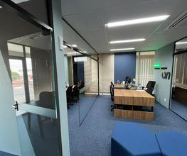 Sala de reunião moderna com mesa de madeira e cadeiras pretas, chão com carpete azul.