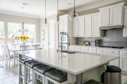 Modern kitchen with white cabinets, island, bar stools, and sunflowers on dining table.