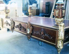 Mesa decorativa de madera con detalles dorados y ruedas, en un taller.