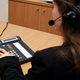 Woman with a headset using a conference call phone at a wooden desk.