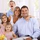 Smiling family of five posing in a bright room with windows and flowers on the table.