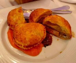 Empanadas doradas sobre salsa naranja en un plato blanco, con cuchillo y tenedor al fondo.