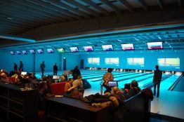 Bowlingbaan met mensen die bowlen; schermen boven de banen tonen scores.