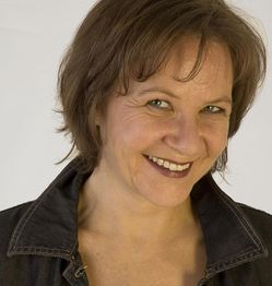 Frau mit kurzem braunem Haar, lächelt in die Kamera. Sie trägt eine dunkle Jeansjacke.