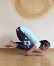 Frau in Yoga-Haltung auf Holzboden vor beiger Wand mit rundem Kunstwerk.