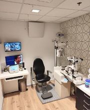 Oogartspraktijk met stoel, meetapparatuur en monitoren aan de muur.