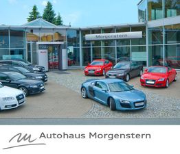 Autos auf einem Hof vor Autohaus Morgenstern mit Glasfassade und Audi-Logo.