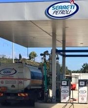 Stazione di servizio con camion cisterna e pompe di benzina sotto tettoia bianca e blu.