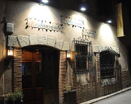 Fachada de un restaurante de noche con luces encendidas y ventanas con rejas decorativas.