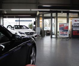 Autohaus-Showroom mit einem schwarzen und einem weißen Auto, umgeben von Verkaufsschildern.