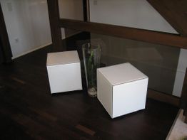Zwei weiße Würfel neben einer Glasvase auf dunklem Holzboden.