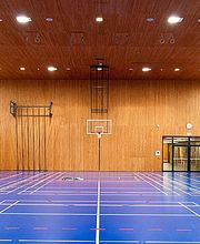 Leere Sporthalle mit blauem Boden, Holzwänden und mehreren Basketballkörben.