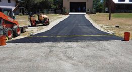 Freshly paved asphalt driveway with construction equipment and caution tape in front of a garage.