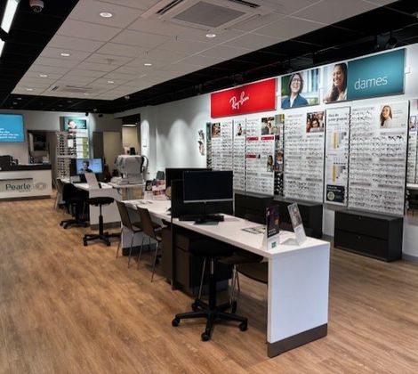 Interieur van een brillenwinkel met houten vloer, tafels en bril displays aan de muren.
