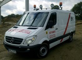 Weißer Mercedes-Transporter mit Aufschrift und Lichtanlage, geparkt auf einer Baustelle.