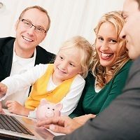 Family smiling and looking at a laptop together, with a piggy bank on the table.