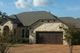 Stone house with dark garage door, gabled roof, and trees in front under a blue sky with clouds.