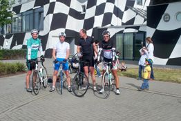 Vier Radfahrer vor einem Gebäude mit schwarz-weißen Mustern.