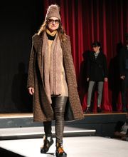 Frau trägt Winterkleidung auf dem Laufsteg: Mantel, Mütze, Schal und Stiefel.