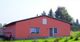Ein einzelnes, rotes Haus mit weißem Fensterrahmen in grüner Umgebung und blauen Himmel.