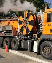 Oranger LKW mit Technik-Aufbau und Schlauch an einem Straßenrand, in Betrieb mit Dampfentwicklung.