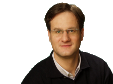 Ein Mann mit Brille und schwarzem Pullover vor einem neutralen Hintergrund.