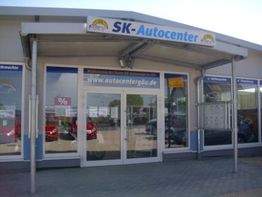 Eingang eines Autohauses mit Schild "SK-Autocenter" und Glastüren, umgeben von Schaufenstern.