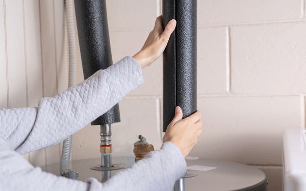 Eine Person dämmt die Wasserrohre ihrer Heizung mit formgerechte Dämmschalen.