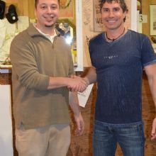 Two men smiling and shaking hands in a casual indoor setting.