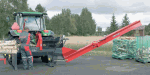 Traktor mit Holzverarbeitungsmaschine und Fließband bei der Arbeit auf einem Landweg.