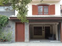 Casa com portão marrom e janelas de madeira, telhado de telhas e árvore ao lado.